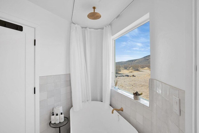 bathroom with a bathing tub, a mountain view, a healthy amount of sunlight, and tile walls