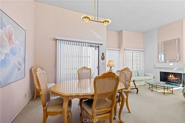 dining room featuring light colored carpet, a wealth of natural light, a brick fireplace, and a textured ceiling