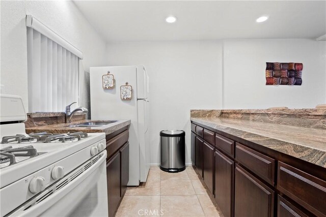 kitchen featuring light tile patterned flooring, dark brown cabinetry, sink, and white gas stove