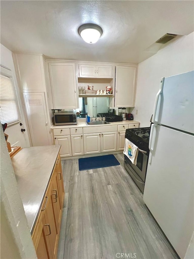 kitchen with sink, light hardwood / wood-style flooring, black electric range oven, white fridge, and white cabinets