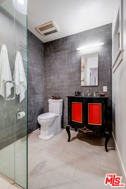 bathroom featuring toilet, vanity, walk in shower, and tile walls