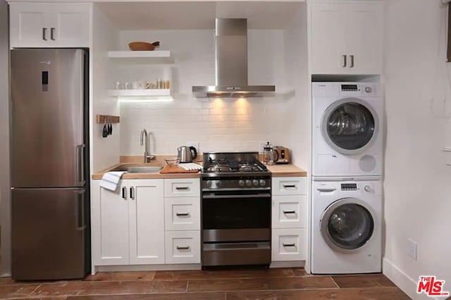 kitchen featuring white cabinets, gas stove, ventilation hood, stacked washer and clothes dryer, and fridge