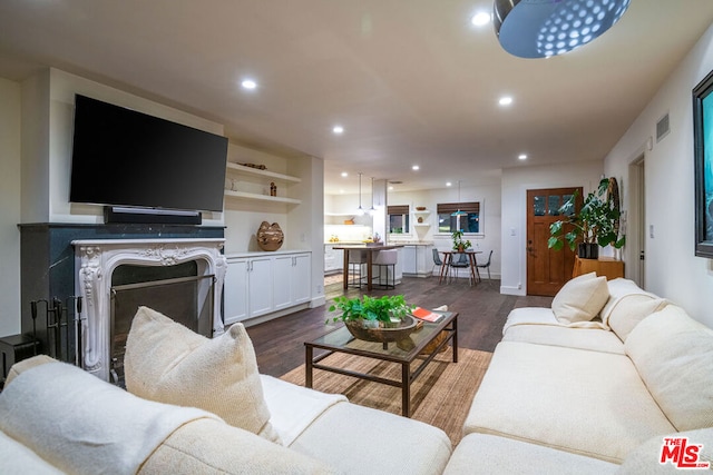 living room with built in shelves, a high end fireplace, and dark hardwood / wood-style flooring