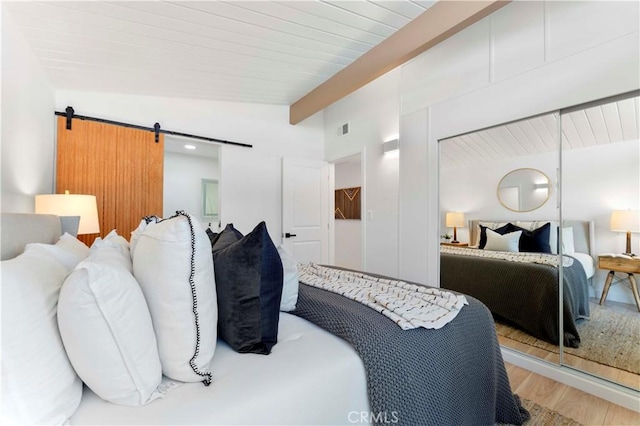 bedroom with hardwood / wood-style floors, lofted ceiling with beams, and a barn door