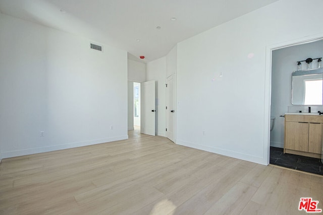 unfurnished bedroom featuring ensuite bath and light hardwood / wood-style flooring