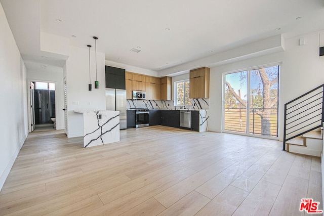 kitchen featuring appliances with stainless steel finishes, a kitchen breakfast bar, a center island, decorative light fixtures, and light wood-type flooring