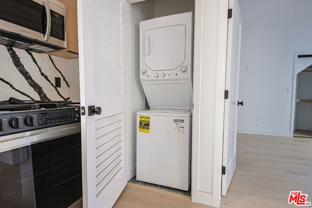 laundry area with stacked washer / drying machine and light hardwood / wood-style flooring