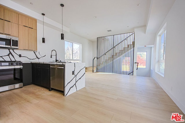 kitchen with sink, decorative backsplash, stainless steel appliances, light stone countertops, and light wood-type flooring