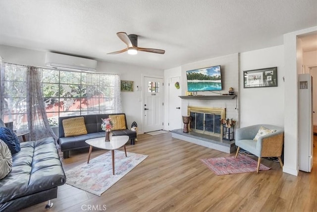 living room with a wall mounted air conditioner, a brick fireplace, ceiling fan, a textured ceiling, and light hardwood / wood-style floors