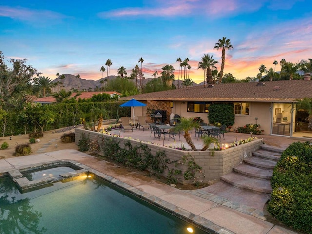 pool at dusk featuring an in ground hot tub, a mountain view, a patio, and a grill