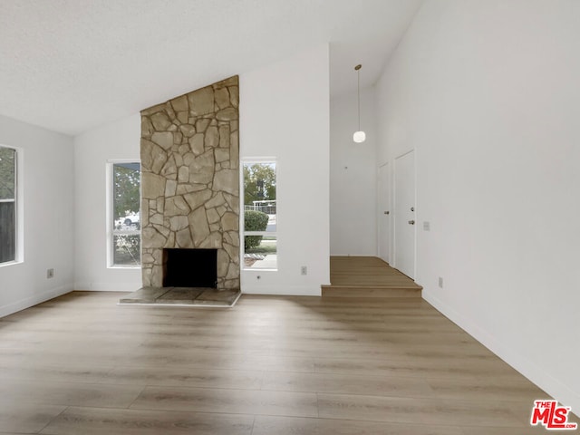 unfurnished living room featuring a fireplace, a textured ceiling, light hardwood / wood-style floors, and high vaulted ceiling