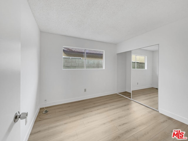 unfurnished bedroom with a closet, a textured ceiling, and light wood-type flooring