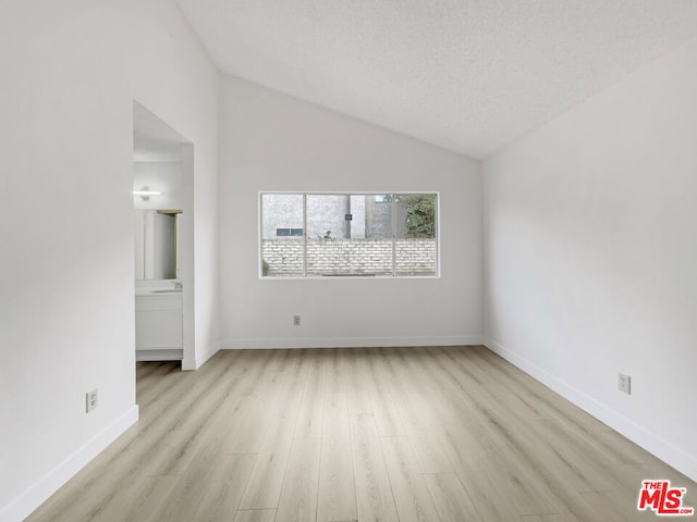 empty room featuring light wood-type flooring, a textured ceiling, and vaulted ceiling