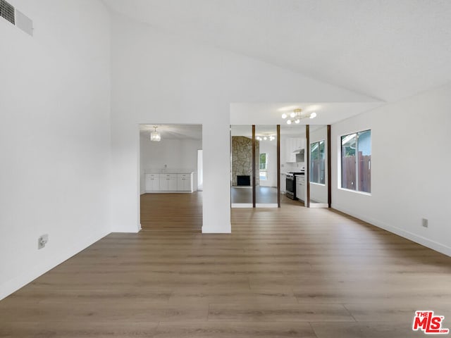 empty room with a fireplace, wood-type flooring, high vaulted ceiling, and a notable chandelier