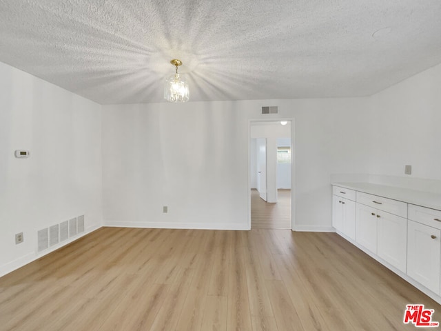 empty room featuring light hardwood / wood-style floors, a textured ceiling, and a chandelier