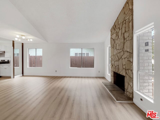 unfurnished living room featuring vaulted ceiling, light hardwood / wood-style flooring, a wealth of natural light, and a stone fireplace