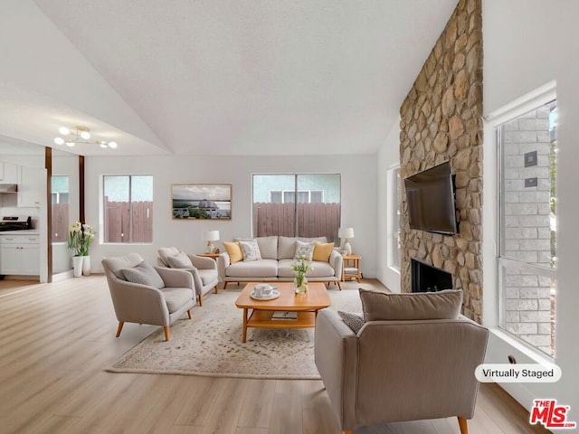 living room featuring light hardwood / wood-style floors, a stone fireplace, plenty of natural light, and lofted ceiling