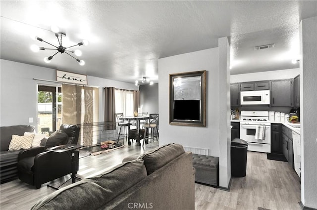 living room with a chandelier, a textured ceiling, and light wood-type flooring