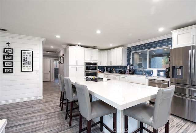 kitchen with appliances with stainless steel finishes, sink, light hardwood / wood-style flooring, white cabinets, and a kitchen island