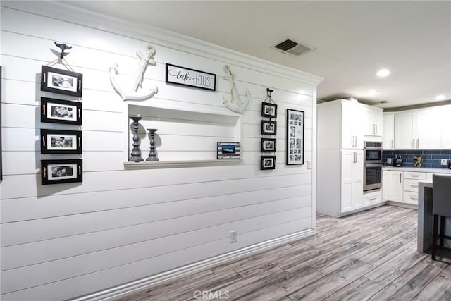 kitchen featuring light wood-type flooring, backsplash, double oven, white cabinets, and wood walls