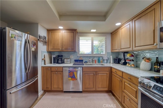 kitchen featuring backsplash, a raised ceiling, sink, and appliances with stainless steel finishes