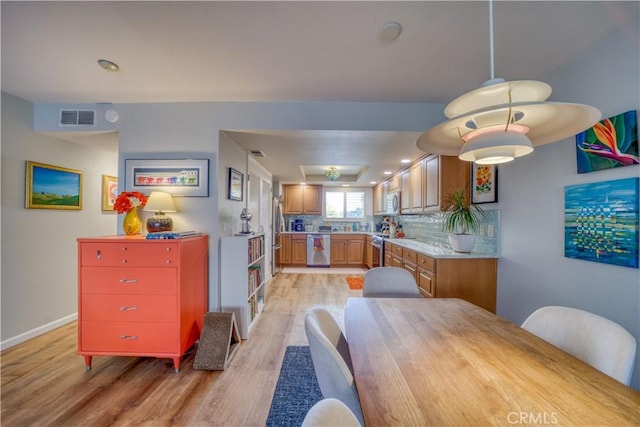 kitchen with pendant lighting, light wood-type flooring, tasteful backsplash, and stainless steel appliances