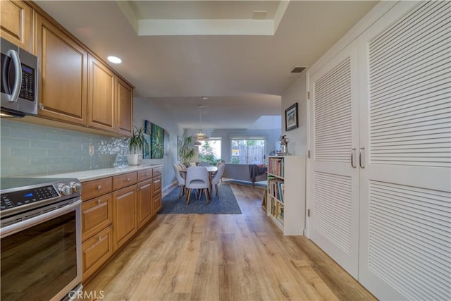 kitchen with stainless steel appliances, tasteful backsplash, light hardwood / wood-style floors, and a tray ceiling