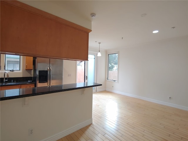 kitchen featuring a breakfast bar, sink, hanging light fixtures, light wood-type flooring, and stainless steel fridge with ice dispenser