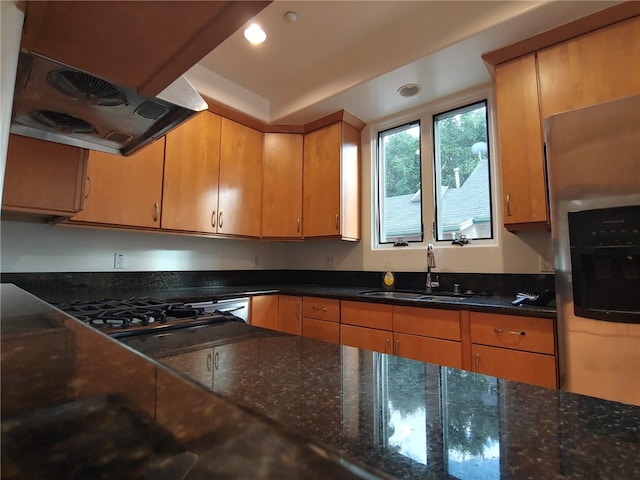 kitchen with stainless steel fridge, dark stone countertops, sink, and range hood