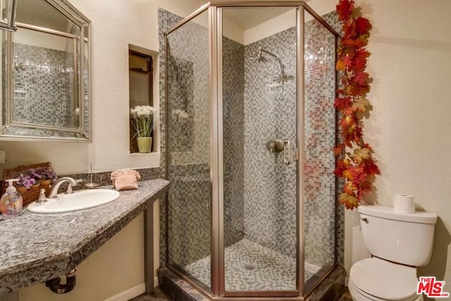 bathroom featuring toilet, a shower with shower door, and sink