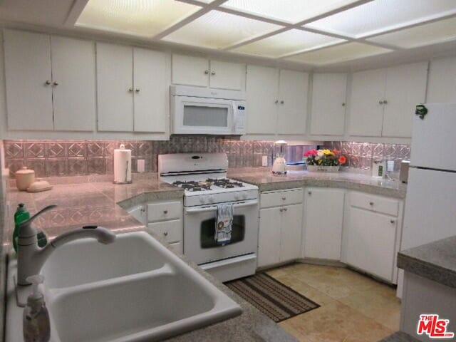 kitchen featuring sink, light tile patterned flooring, white appliances, decorative backsplash, and white cabinets