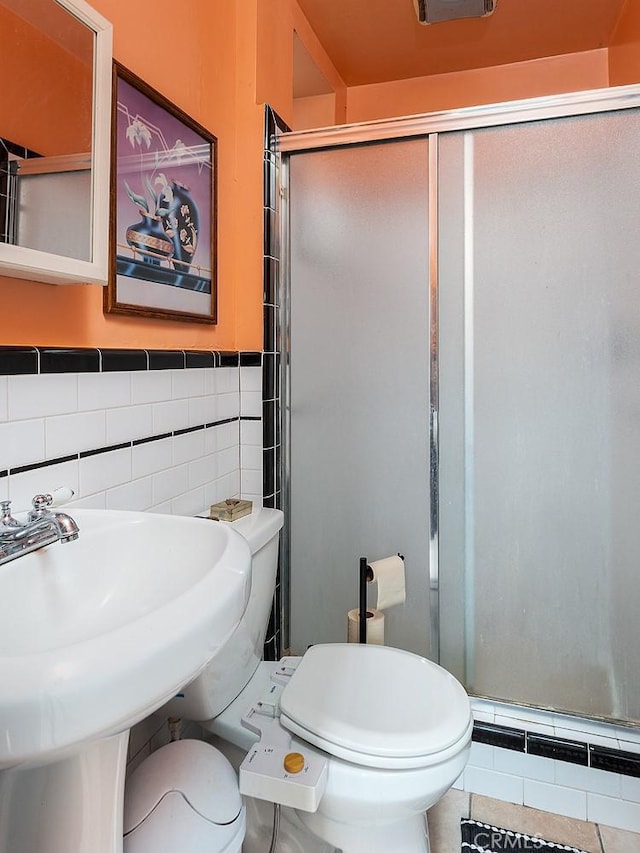 bathroom with tile patterned floors, an enclosed shower, sink, tile walls, and toilet