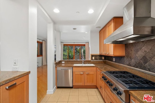 kitchen featuring wall chimney range hood, light tile patterned floors, sink, stainless steel appliances, and tasteful backsplash