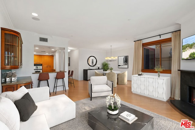 living room featuring ornamental molding, light wood-type flooring, and a notable chandelier