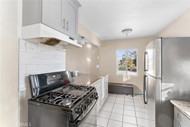 kitchen with stainless steel fridge, backsplash, light stone counters, black gas range oven, and light tile patterned floors