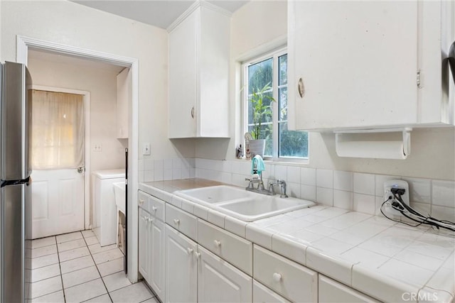 kitchen featuring sink, light tile patterned floors, tile counters, white cabinetry, and stainless steel refrigerator