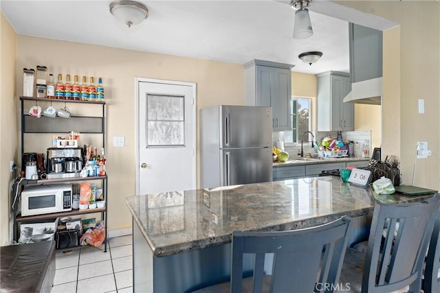 kitchen featuring dark stone counters, sink, gray cabinets, stainless steel fridge, and kitchen peninsula