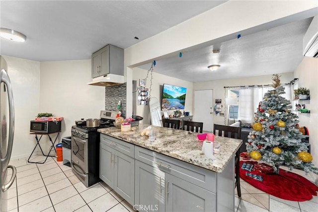 kitchen featuring gray cabinetry, light tile patterned floors, appliances with stainless steel finishes, tasteful backsplash, and a breakfast bar area