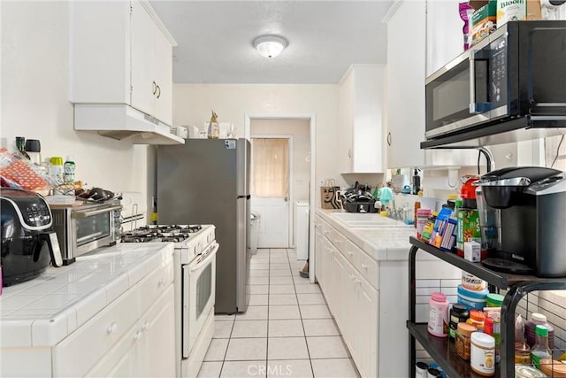 kitchen with white range with gas stovetop, sink, light tile patterned floors, tile counters, and white cabinetry