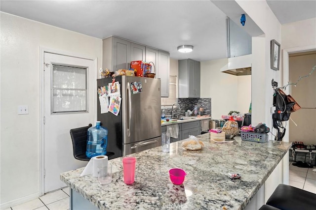 kitchen with gray cabinetry, light stone countertops, sink, stainless steel fridge, and light tile patterned floors