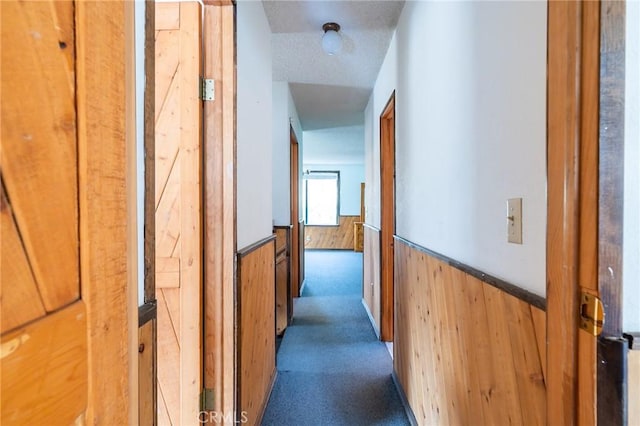 hall with wood walls, dark carpet, and a textured ceiling