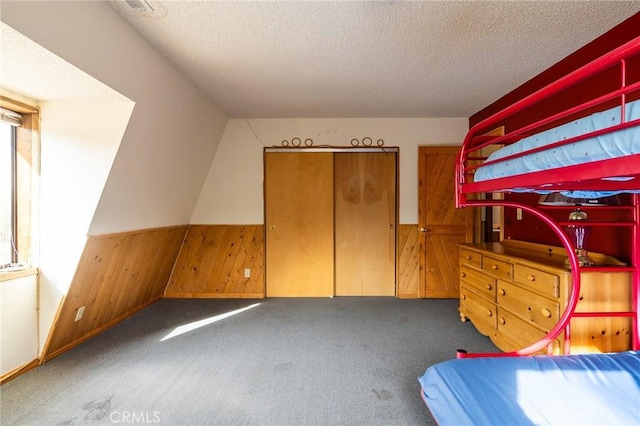 unfurnished bedroom featuring dark colored carpet, a textured ceiling, a closet, and wood walls