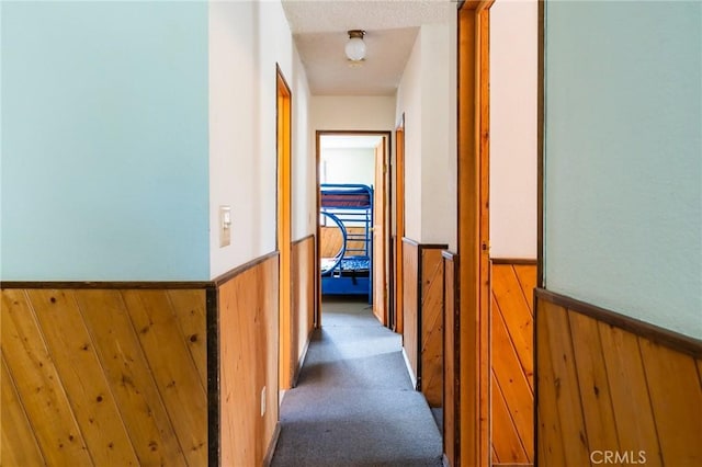 hall featuring carpet flooring, wood walls, and a textured ceiling