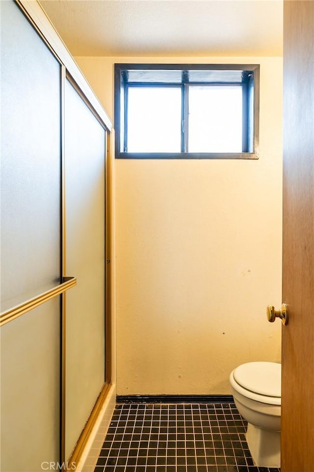 bathroom featuring tile patterned flooring, a healthy amount of sunlight, a shower with shower door, and toilet