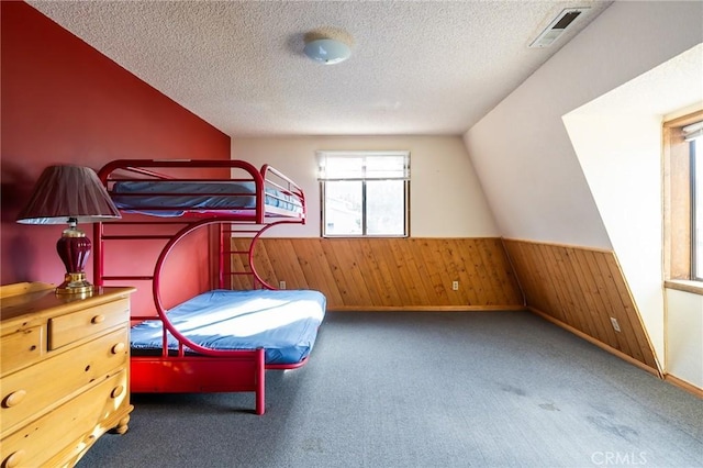 carpeted bedroom featuring lofted ceiling, a textured ceiling, and wooden walls