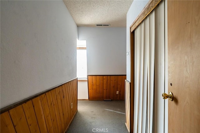 hall featuring wood walls, carpet floors, and a textured ceiling