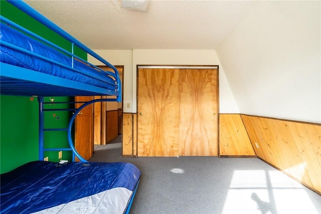 bedroom with carpet, a textured ceiling, a closet, and wood walls