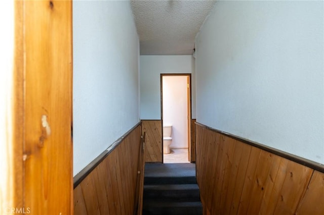 stairs with wood walls and a textured ceiling