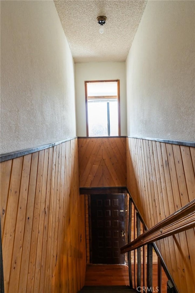 stairway with a textured ceiling, hardwood / wood-style flooring, and wood walls