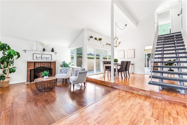 living room featuring high vaulted ceiling, hardwood / wood-style flooring, a brick fireplace, and a notable chandelier